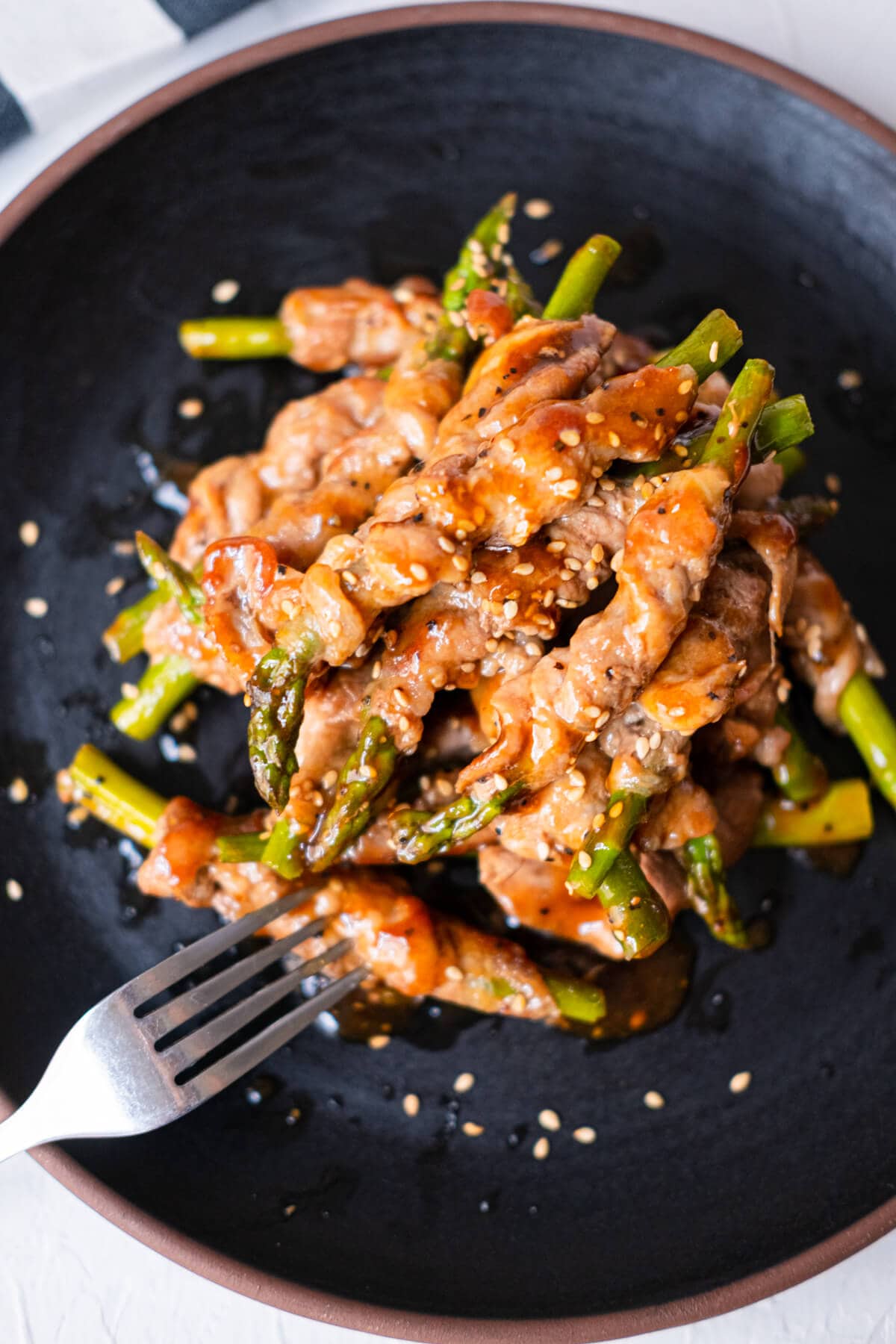 Pork wrapped asparagus in a black shallow plate with a fork on the side. 