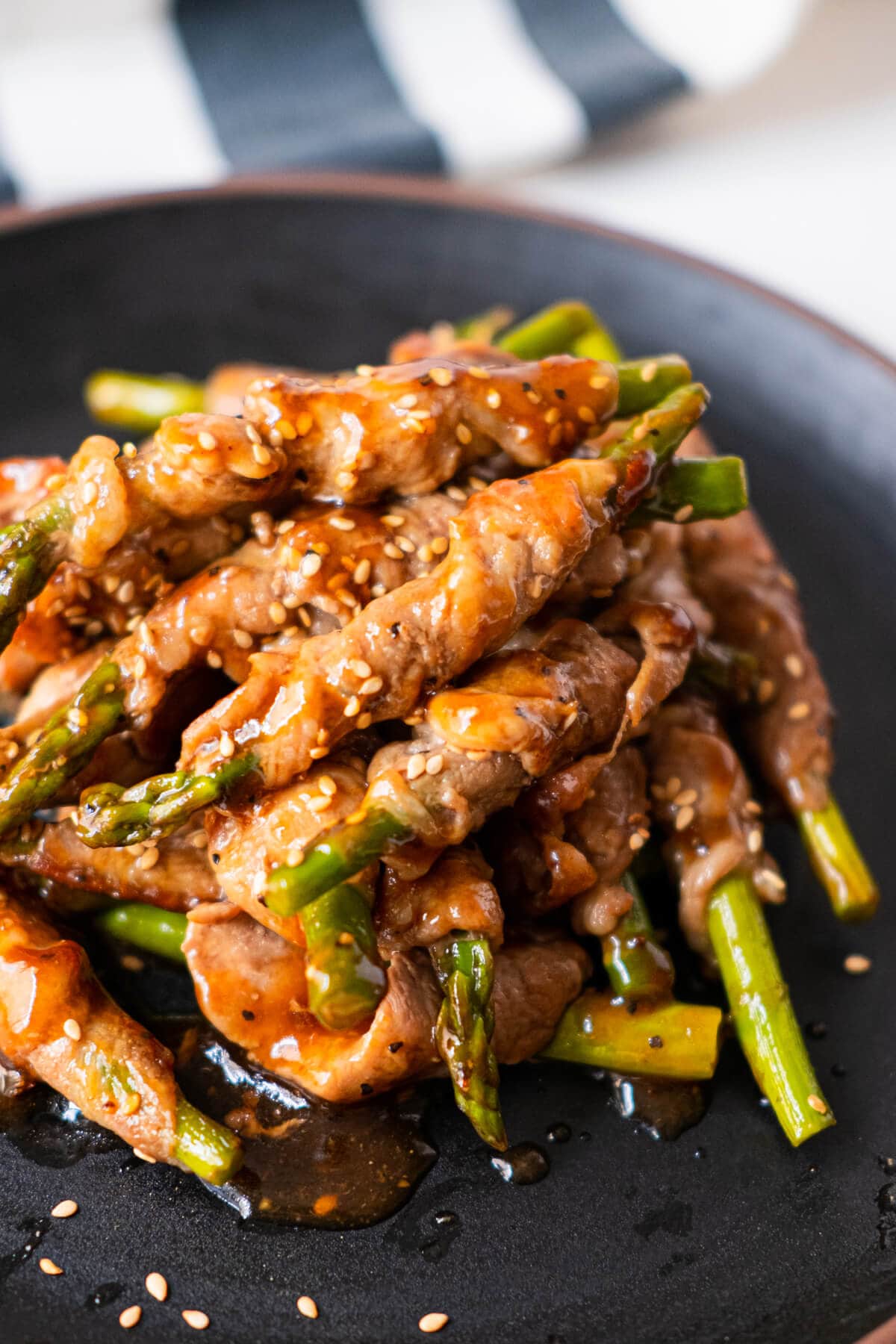 Hot thinly sliced black pepper sauce coated pork wrapped around asparagus served in a black plate with white sesame sprinkled on top. 