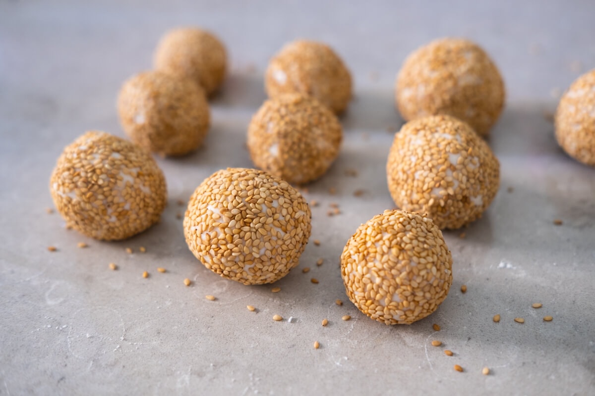 Balls of white sesame coated doughs on baking paper. 