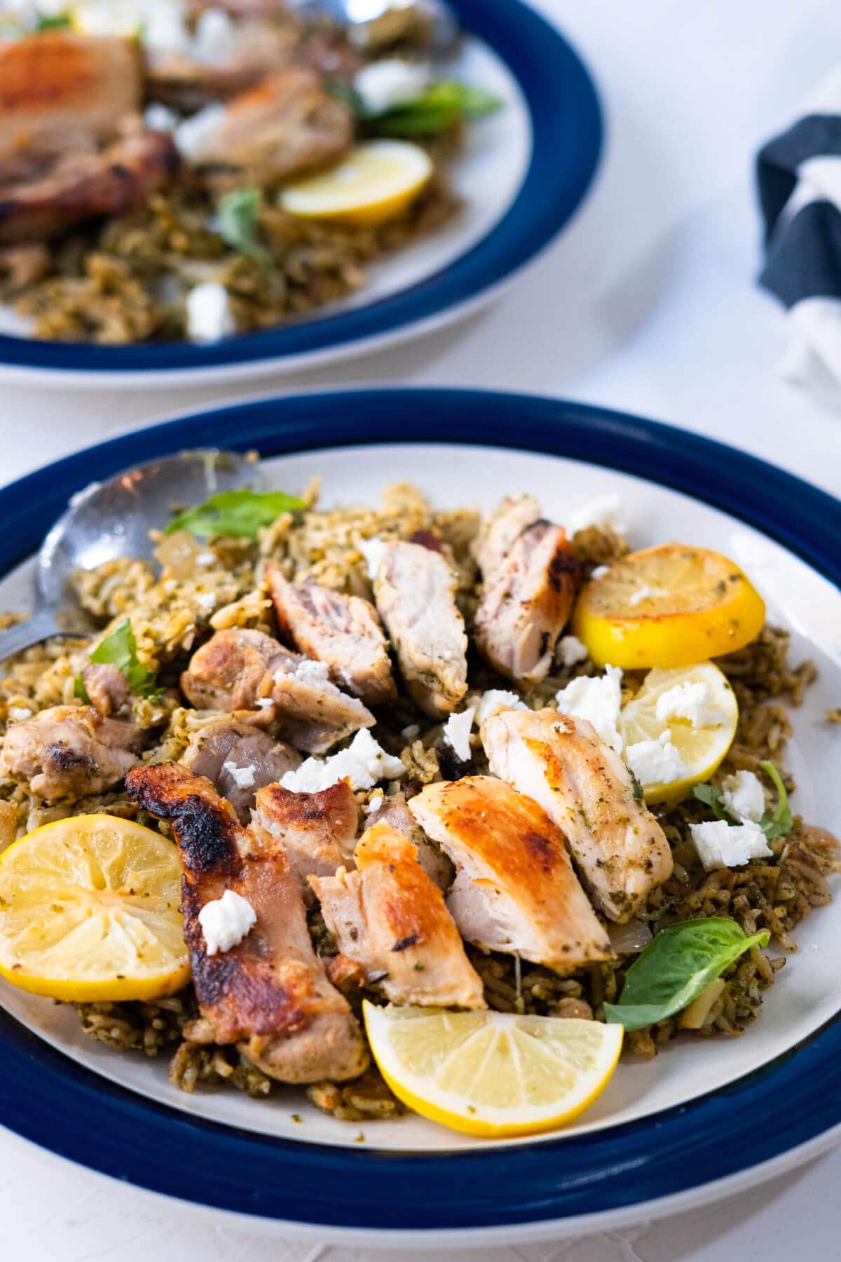 A plate of spinach sauce coated rice wth greek chicken, feta cheese, and lemon on top. 