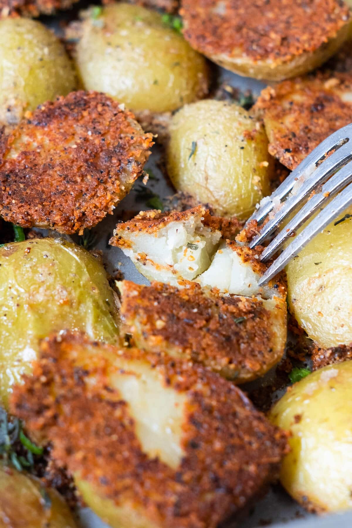 Fork poking into the tender potatoes in a baking tray. 