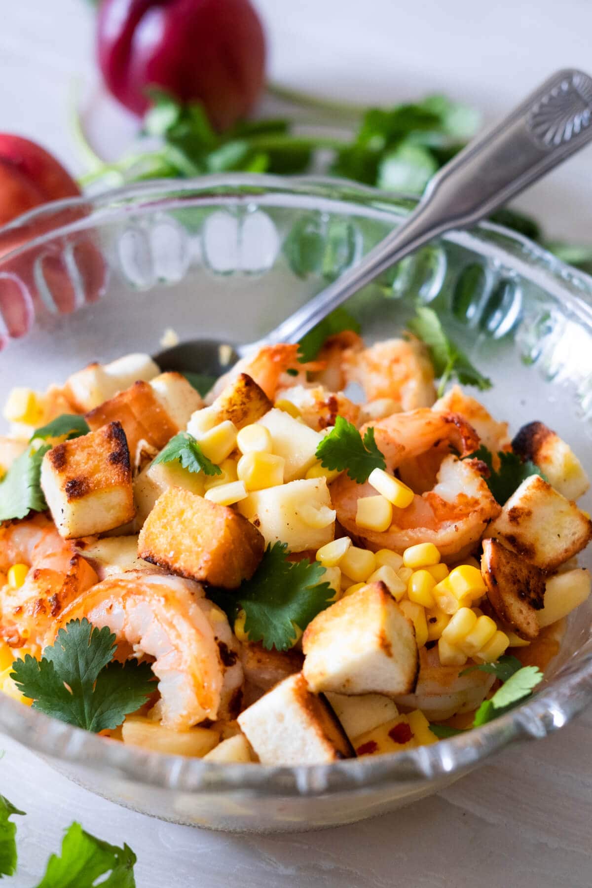 A bowl of prawns, peaches, topped with sweet corn, crountons and cilantro leaves. 