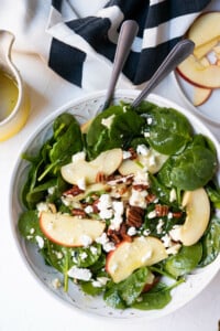 Spinach salad with three toppings, apple slices, chopped pecans and feta cheese crumbles.