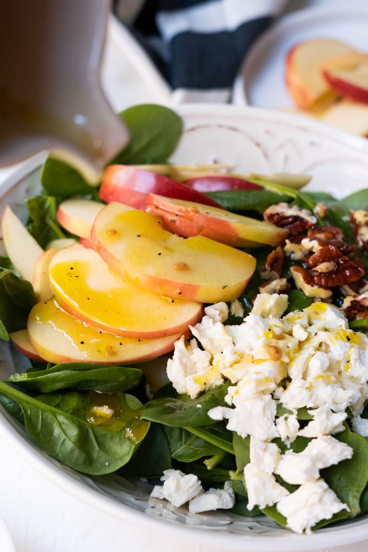 Close up on crisp apple slices over spinach salad and vinaigrette dressing drizzled on top. 