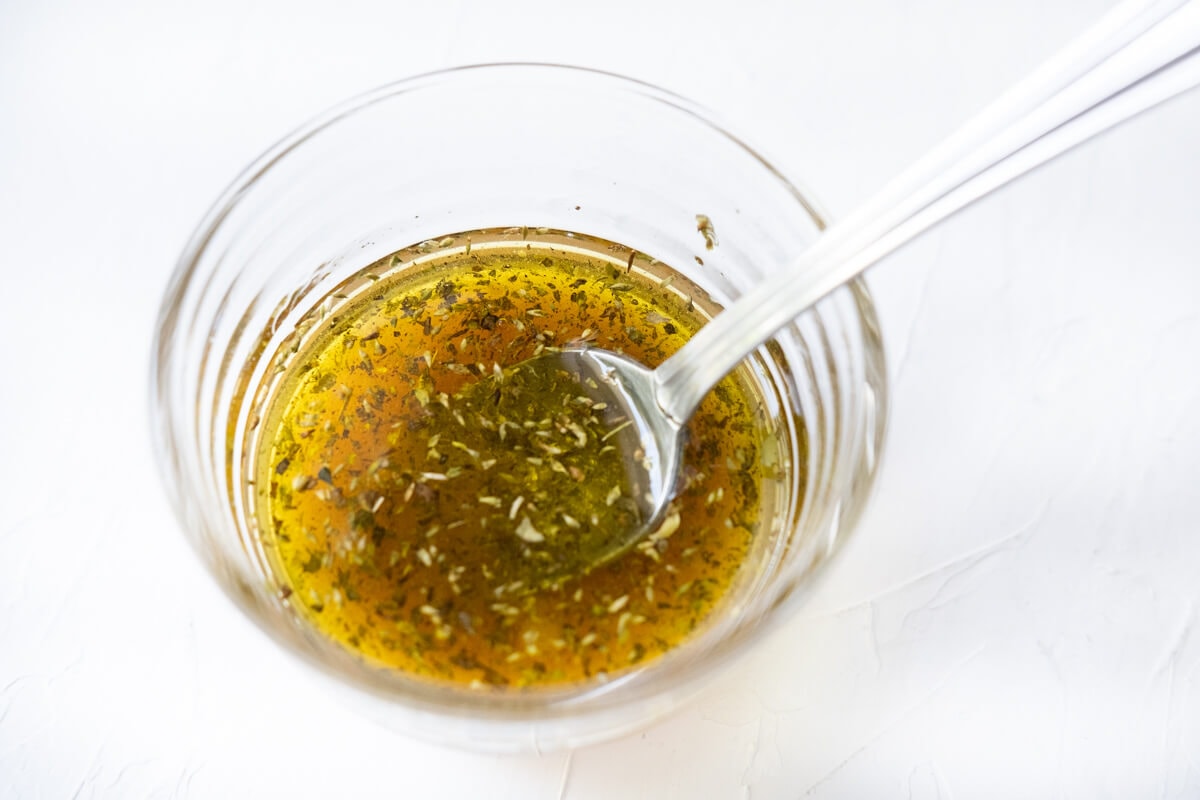 Homemade vinaigrette in a glass bowl with a spoon in it. 