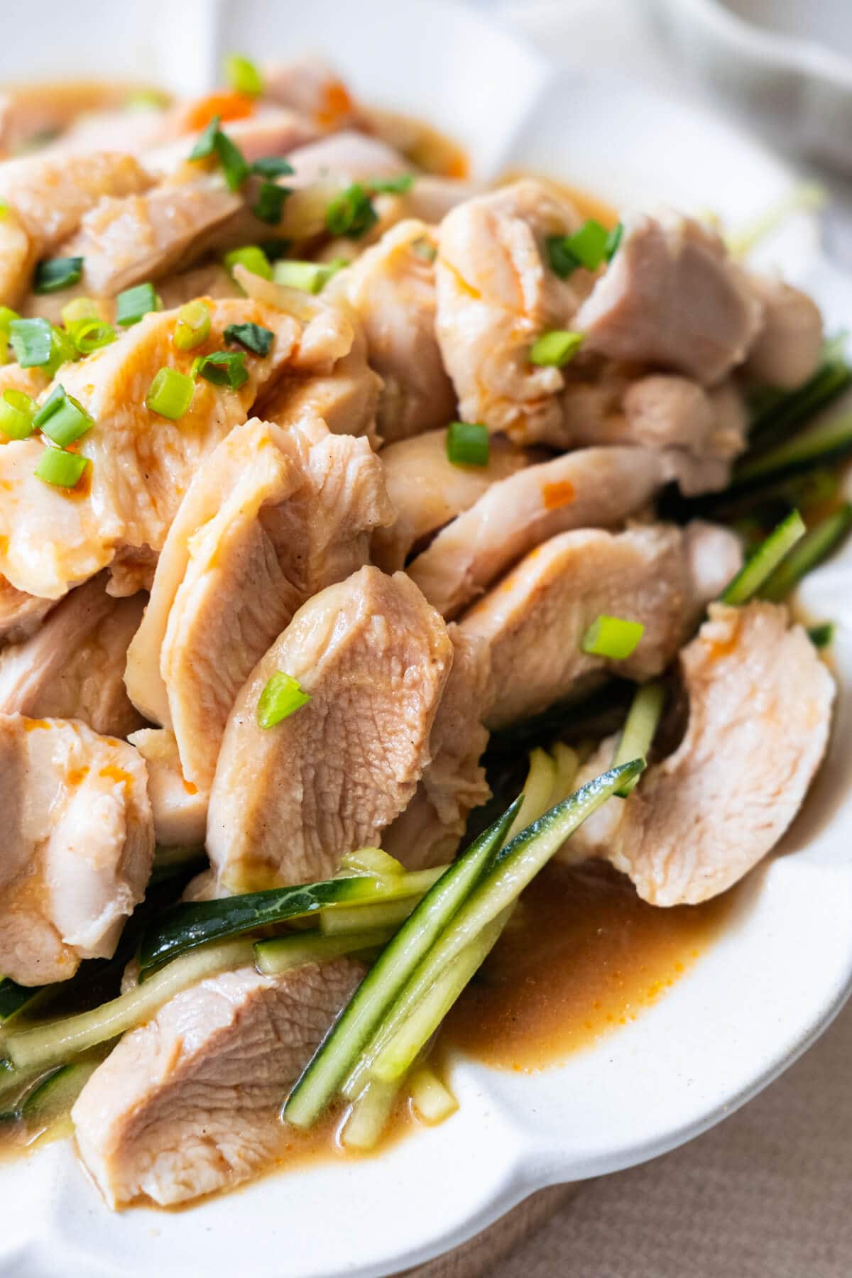 Close up shot of tender, juicy chicken thigh meat coated with sesame sauce with cucumber lay on the bottom. 