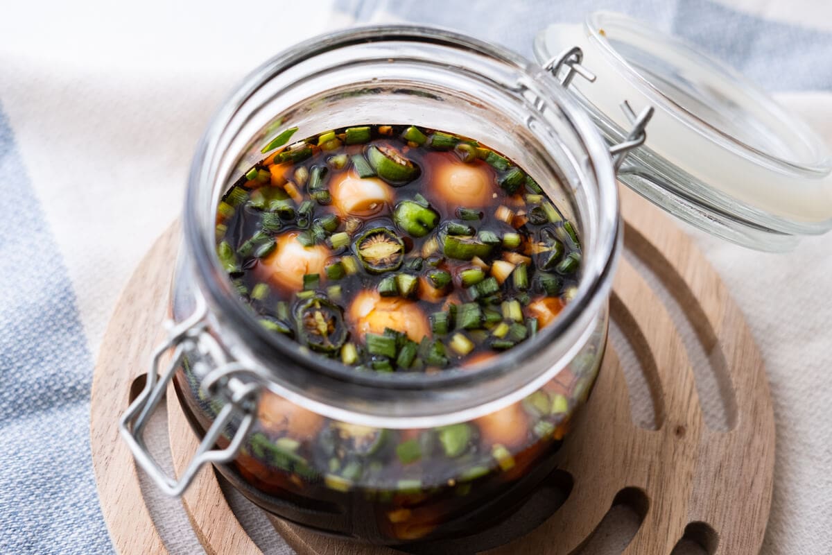 Boiled and peeled quail eggs soaked in soy sauce with green onion and chili pepper in a mason jar. 