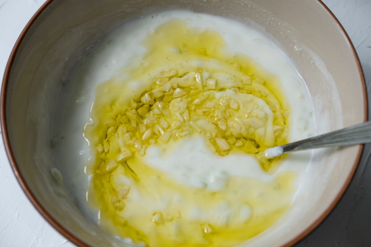 Combined white greek yogurt with olive oil and garlic mix, and cucumber in a bowl. 