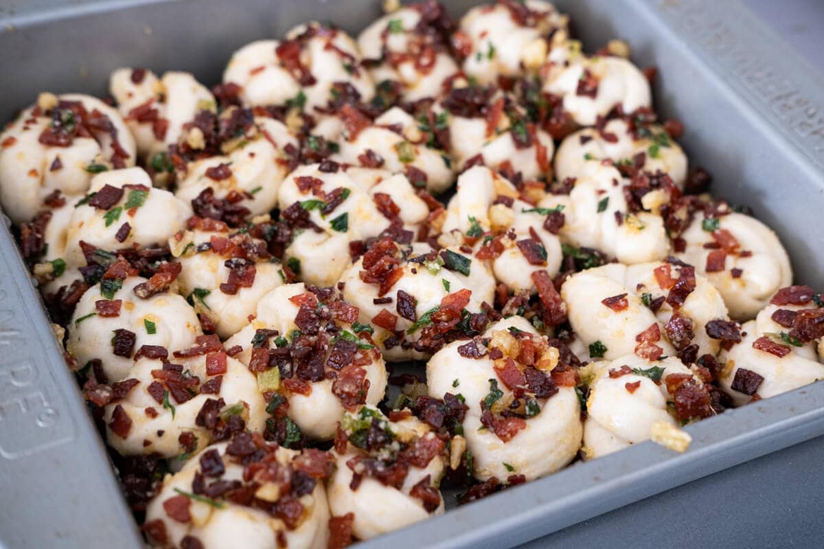 Dough knots coated with pepperoni mixture in a baking tray. 