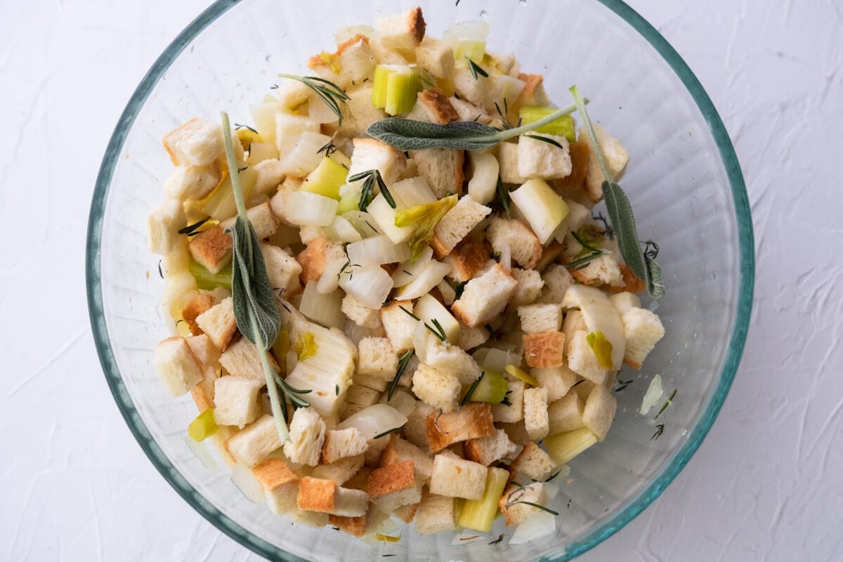 Dried bread cubes, fresh herbs combined with onion, celery with melted butter in a glass bowl. 