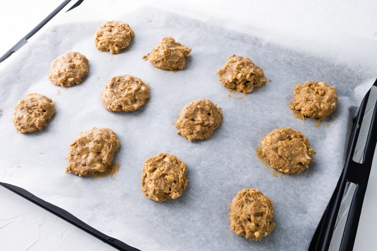 Brown cookie doughs on a baking sheet lined with parchment paper on oven tray. 