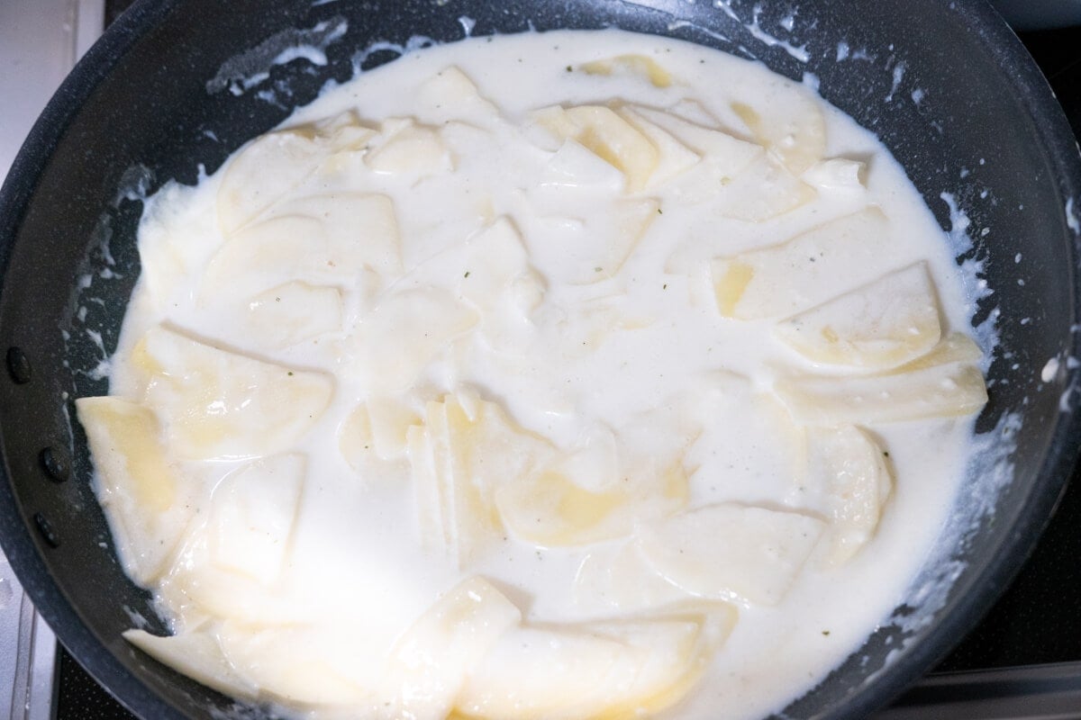 Sliced potatoes covered in white creamy sauce in a skillet. 