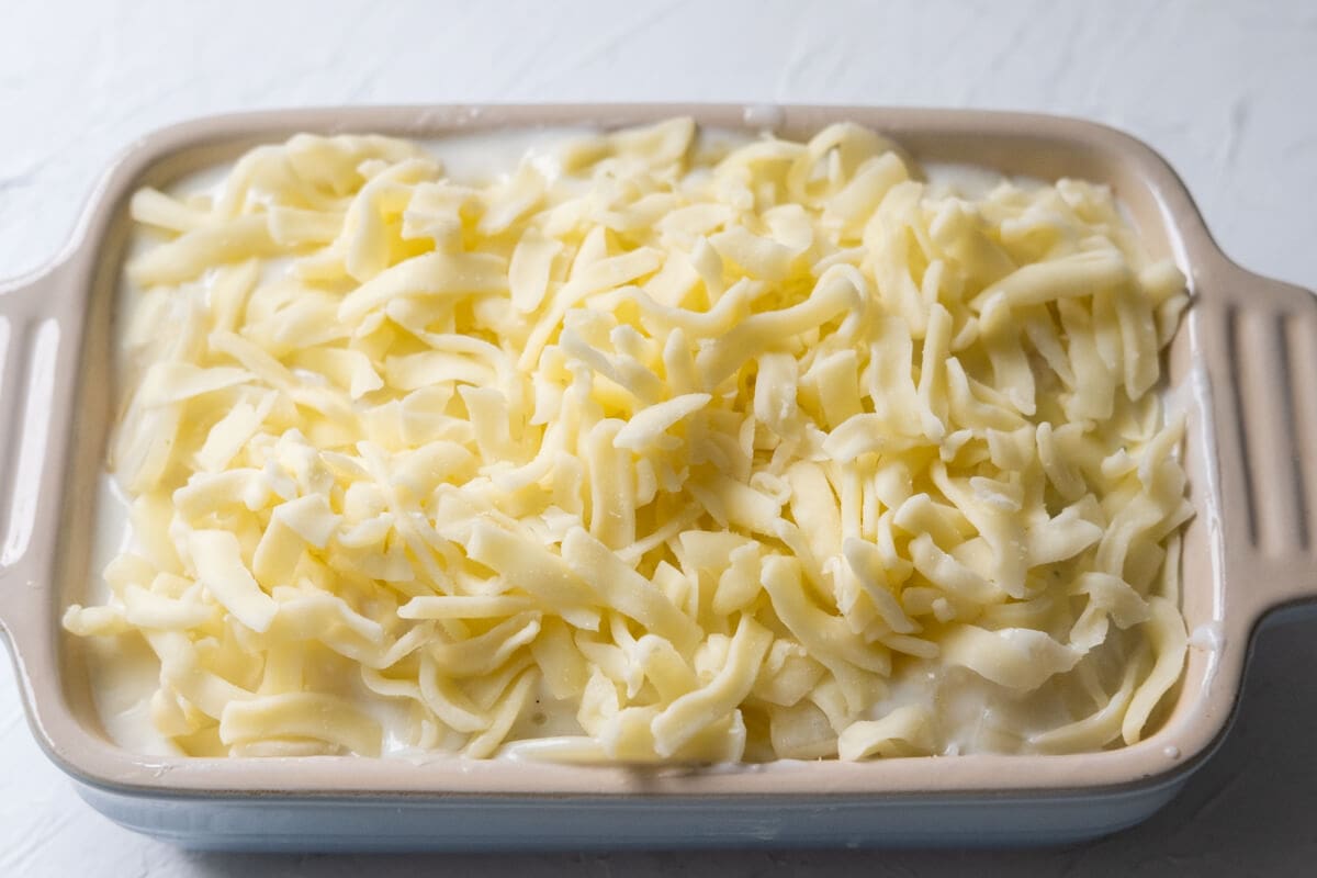 Cooked potato slices covered with white sauce topped with mozzarella cheese in a baking dish. 