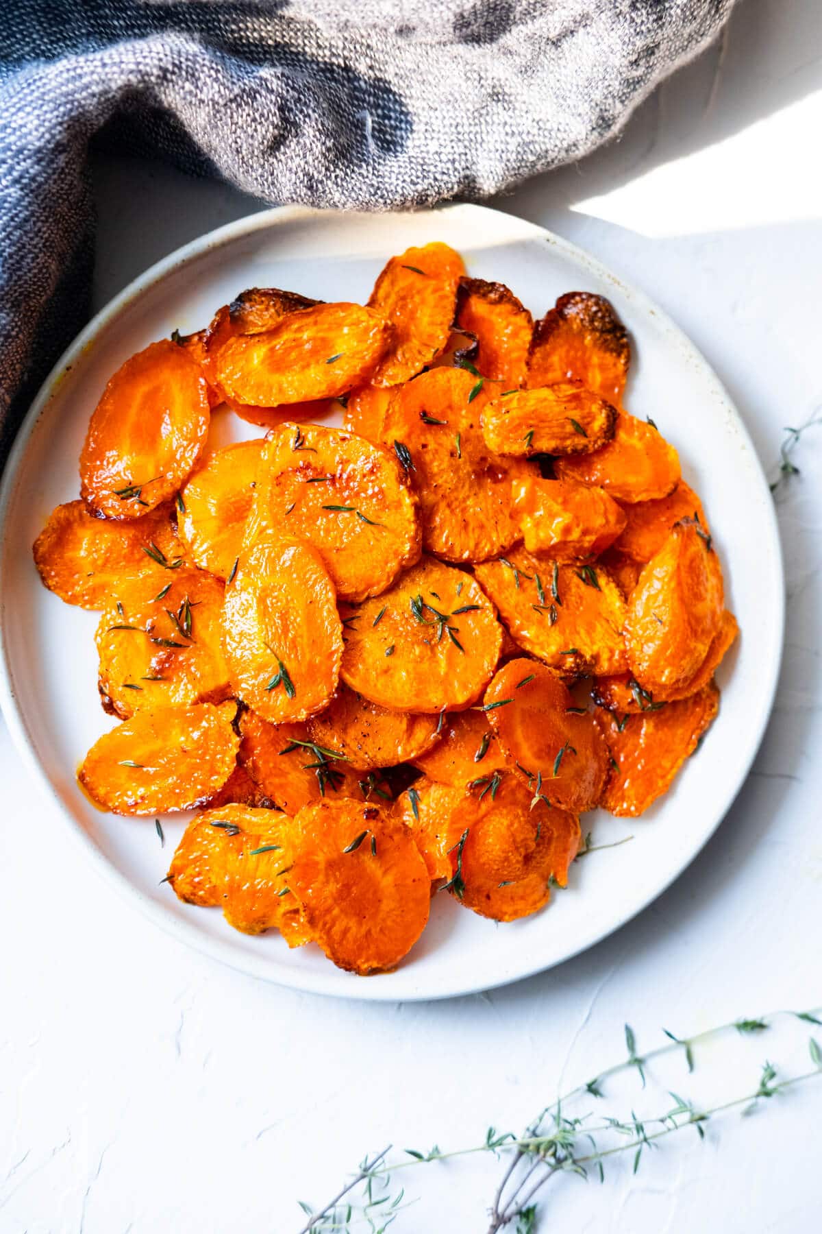 Roasted carrots with thyme served in a white shallow plate.