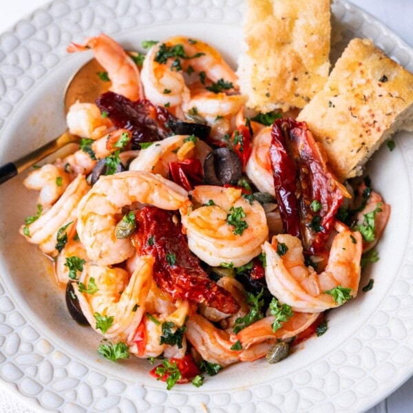 Mediterranean olive and shrimp in a shallow plate with 2 pieces of focaccia on the side.