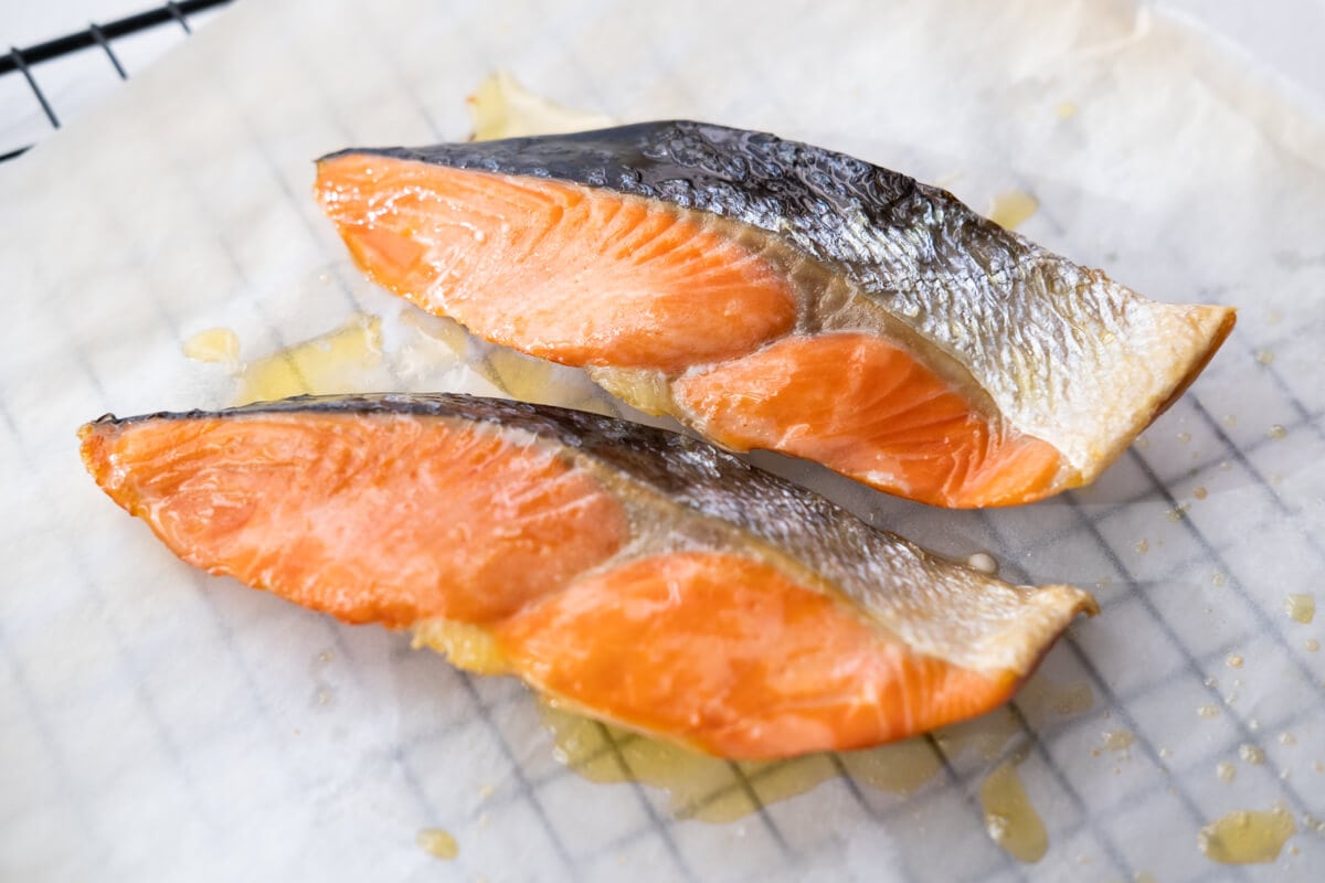 Two slices of baked salmon on the parchment paper. 