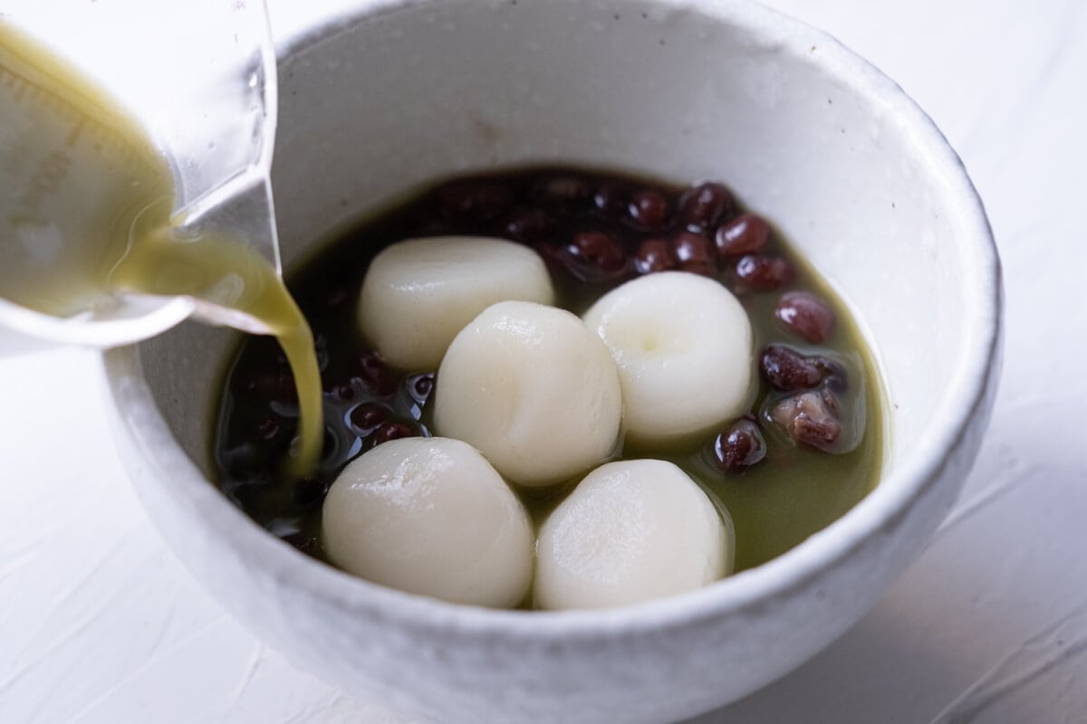 Pouring the matcha tea into a bowl filled with red bean paste and shiratama dango.