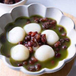 Matcha zenzai served in a small bowl with red bean paste, shiratama dango and matcha tea.