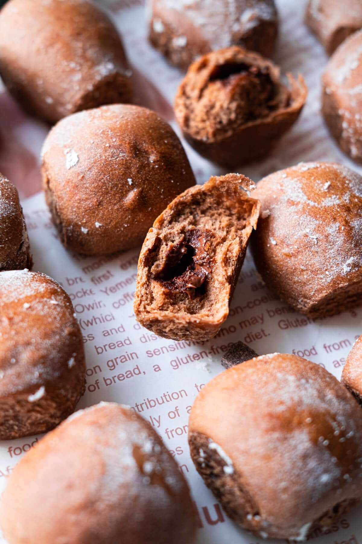 Chocolate milk buns arranged on the baking sheet with one buns showing the molten chocolate filling in the center.