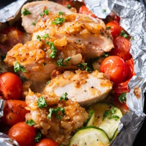 Tender chicken breasts with honey mustard sauce on top alongside cherry tomatoes and zucchini slices.