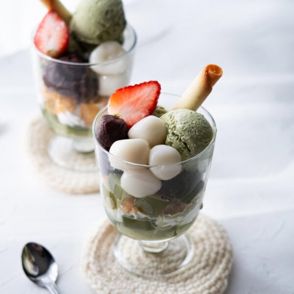 Matcha parfait layered with whipped cream, matcha jelly, mochi, sweet red bean paste, and topped with matcha ice cream, strawberry and cookie.