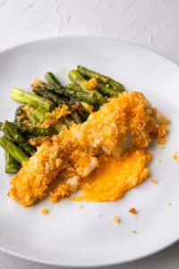 Baked sea bass fillet with golden brown crispy panko on top alongside asparagus.