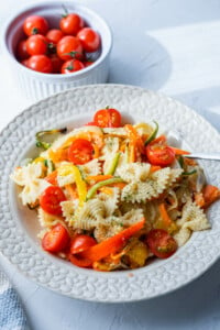 Pasta primavera served in a large plate alongside a bowl of fresh cherry tomatoes.