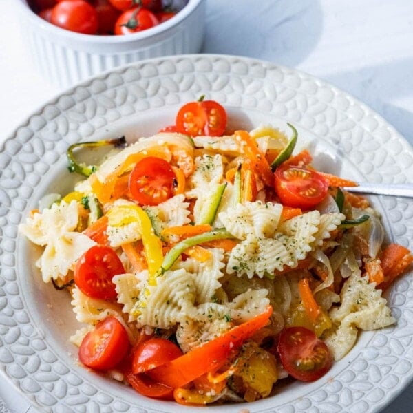 Pasta primavera served in a large plate alongside a bowl of fresh cherry tomatoes.