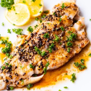 Buttery black pepper fish with chopped parsley on top and lemon slices aside.