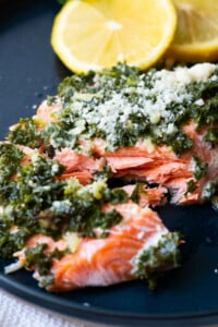 Flaky salmon topped with parsley parmesan on top and sliced lemon aside.