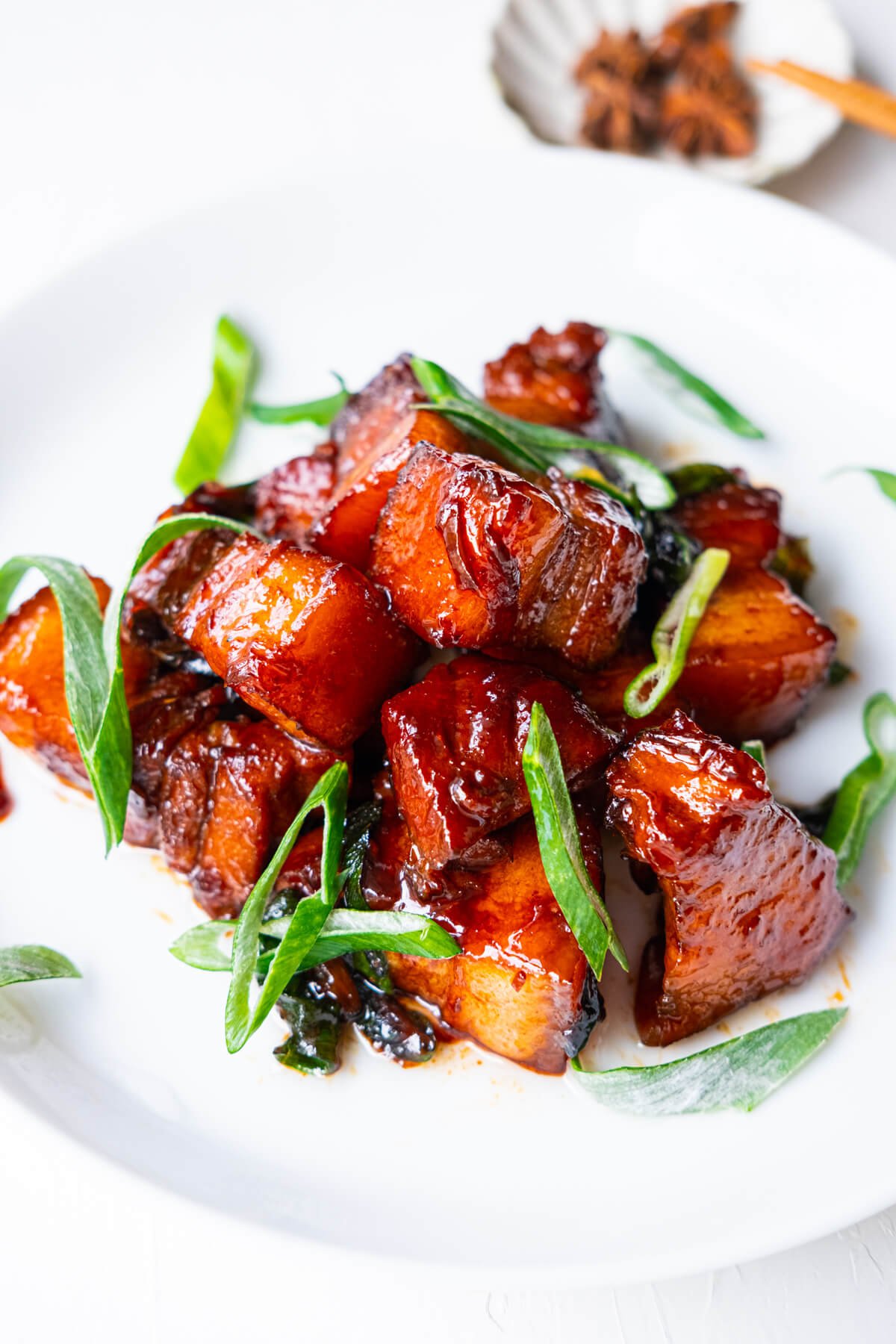 Braised pork belly on a white plate with star anise placed on a small dish on the side. 