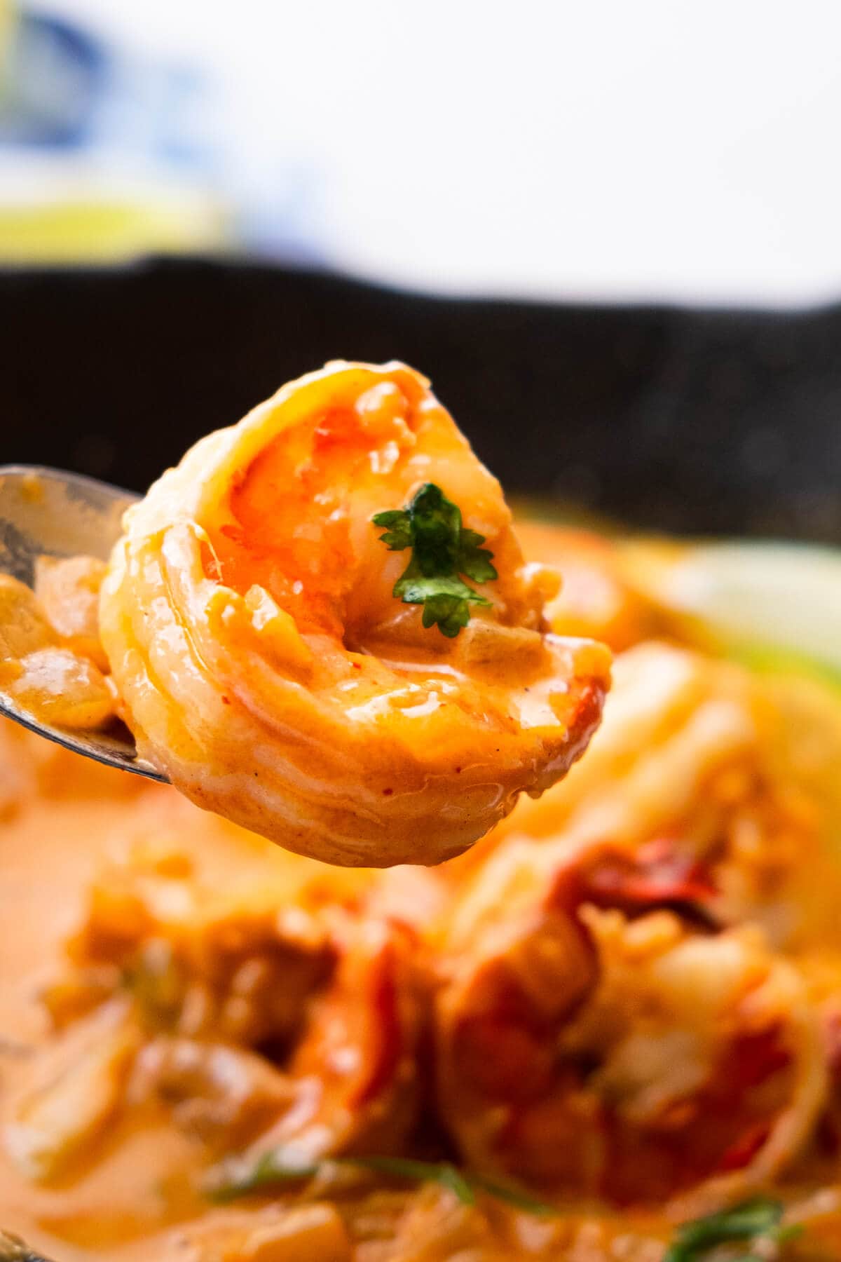 A shrimp in a spoon with cilantro leave on top.  