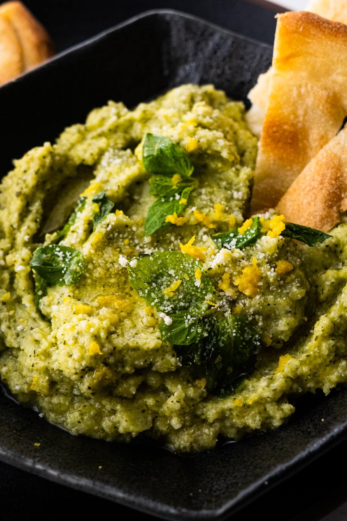 Zucchini dip with olive oil drizzled on top and served in a black plate. 