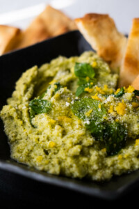 Creamy zucchini dip topped with mint leaves, lemon zest, grated parmesan and thin slices of bread.