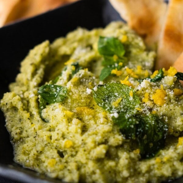 Creamy zucchini dip topped with mint leaves, lemon zest, grated parmesan and thin slices of bread.