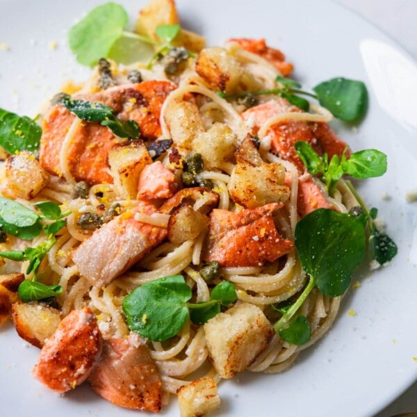 Salmon spaghetti coated with creamy lemon and garlic sauce, and served in a plate with crispy sourdough bread, baby capers and watercress leaves sprinkled on top.