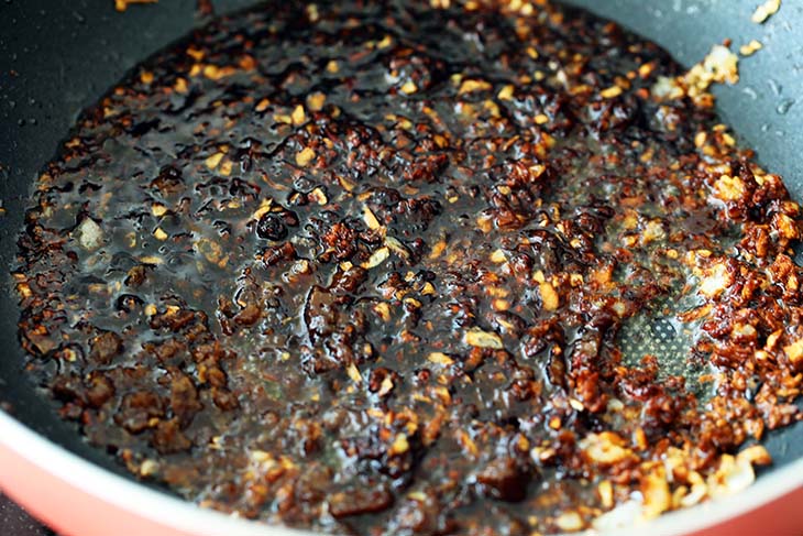 Taucheo, dark soy sauce and palm sugar added to minced garlic in a pan. 