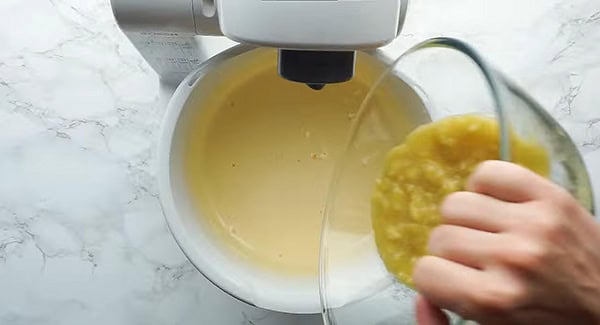 Mashed bananas being mixed into the beaten eggs and sugar mixture.