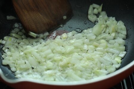 Making chicken curry by sauteing onion in a pan. 