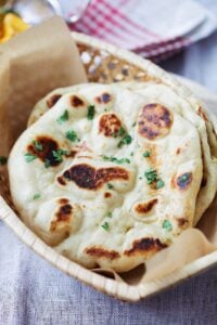 Fluffy and chewy naan with brown bubbly blisters in a bread basket.