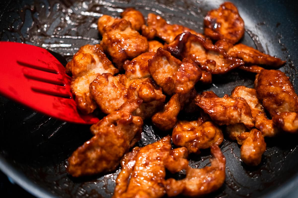 Stir-frying Peking pork with red sauce in a pan. 