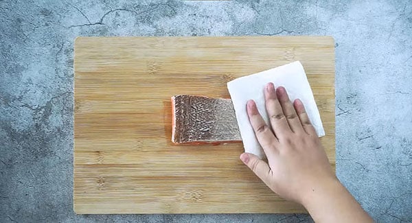 Patting dry a salmon fillet with tissue.