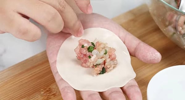 Adding pork filling on a dumpling wrapper. 