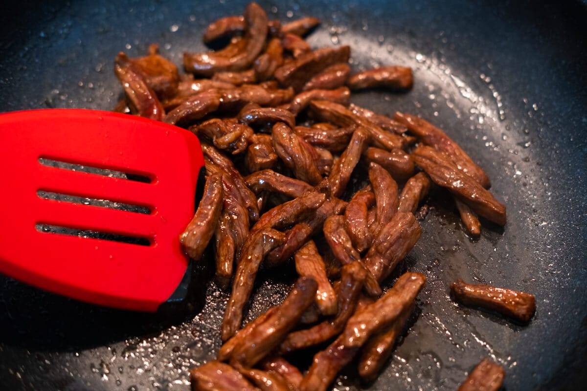 Stir fry marinated beef in a pan. 