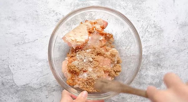 Chicken thighs, brown sugar, salt, cayenne pepper in a bowl mixed using a spatula. 