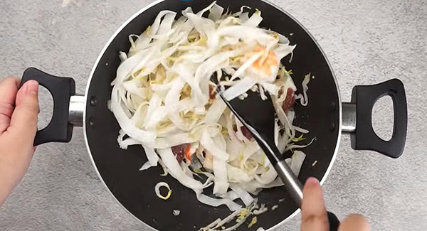 Flat noodles added into a wok with bean sprouts, garlic, shrimp and Chinese sausage. 