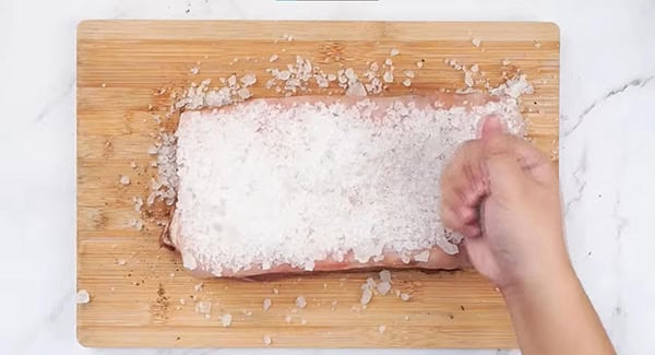 Kosher salt is layered evenly on top of the pork belly. 