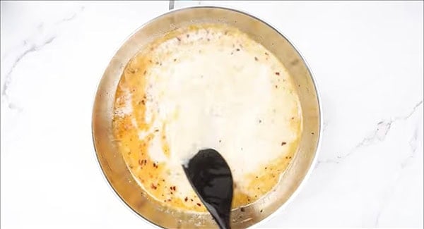 Creamy pasta sauce ingredients in a skillet being stirred with a spatula. 