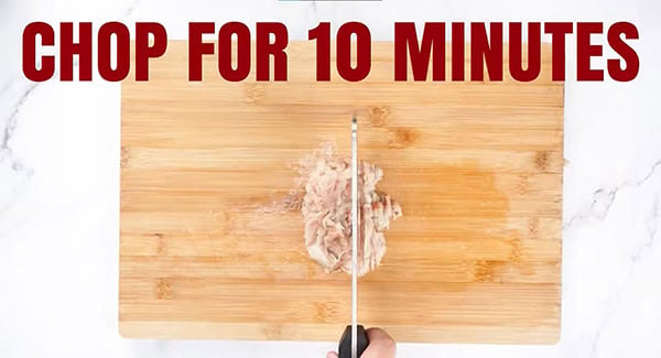 Fish meat being chopped with a cleaver on a chopping board. 