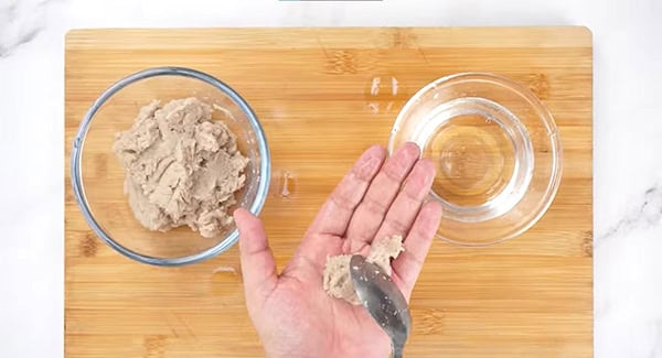 Fish paste is placed into the palm using a spoon. 